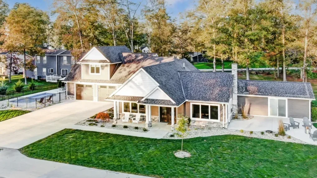 A large modern house with a dark gray roof, surrounded by a lush green lawn and landscaped yard, with multiple outdoor seating areas and a swimming pool in the backyard.