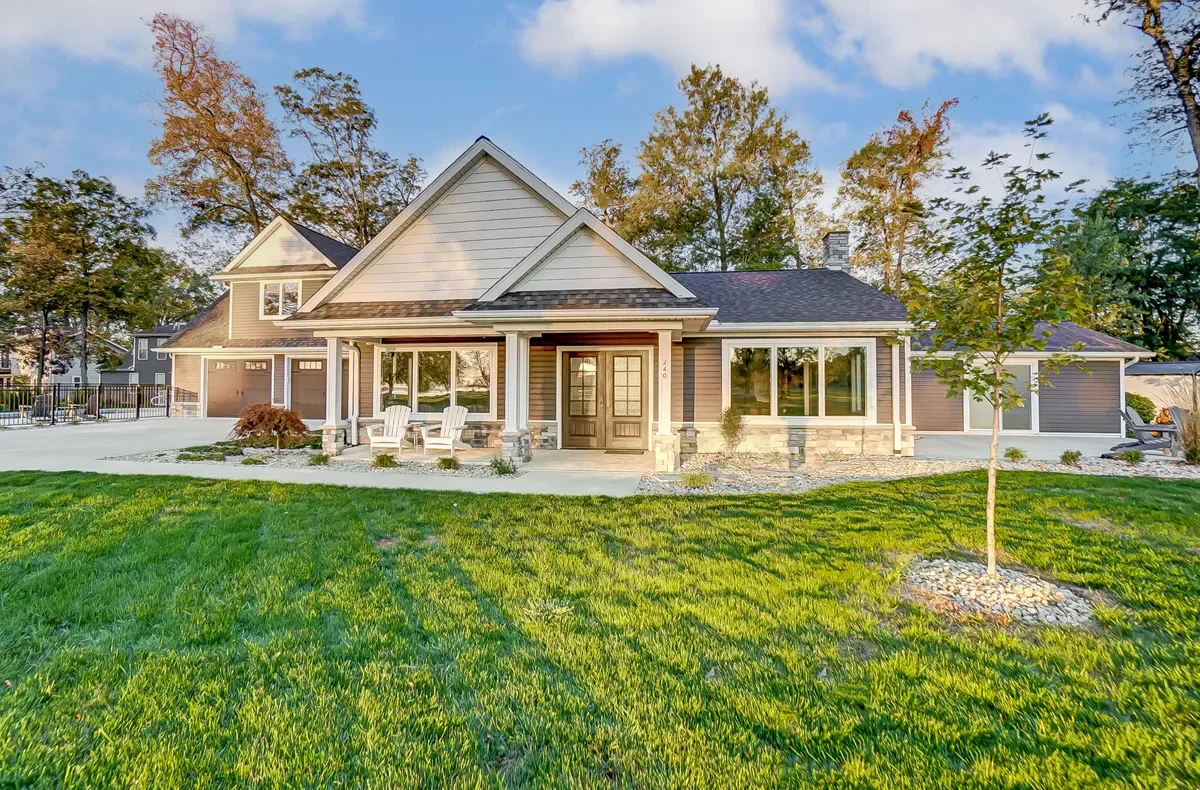 A front view of a modern house with a well-manicured lawn and trees in the background, during daytime.
