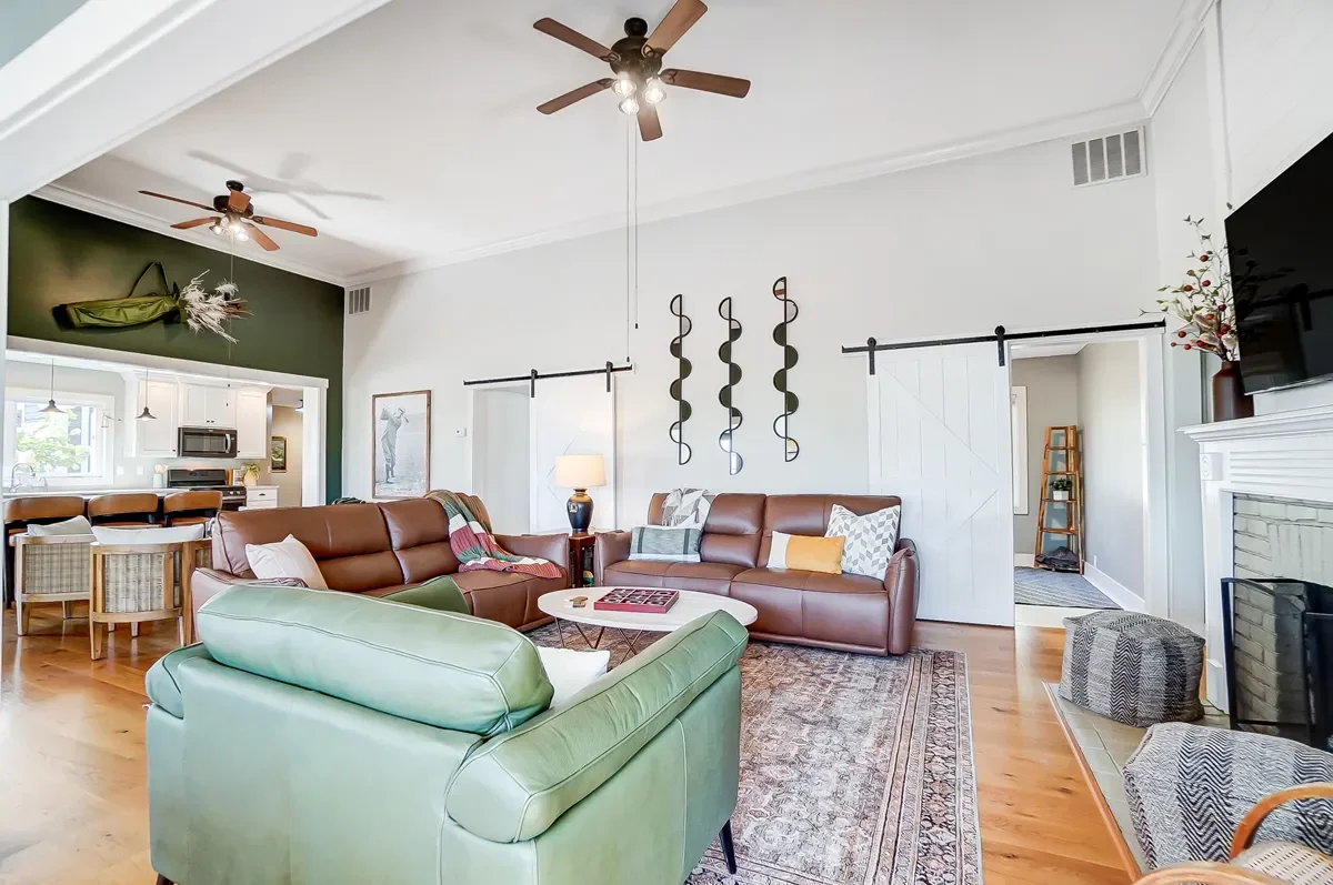 Living room with leather sofas, a green armchair, a coffee table, and wall decor, with a view into the kitchen area in the background.