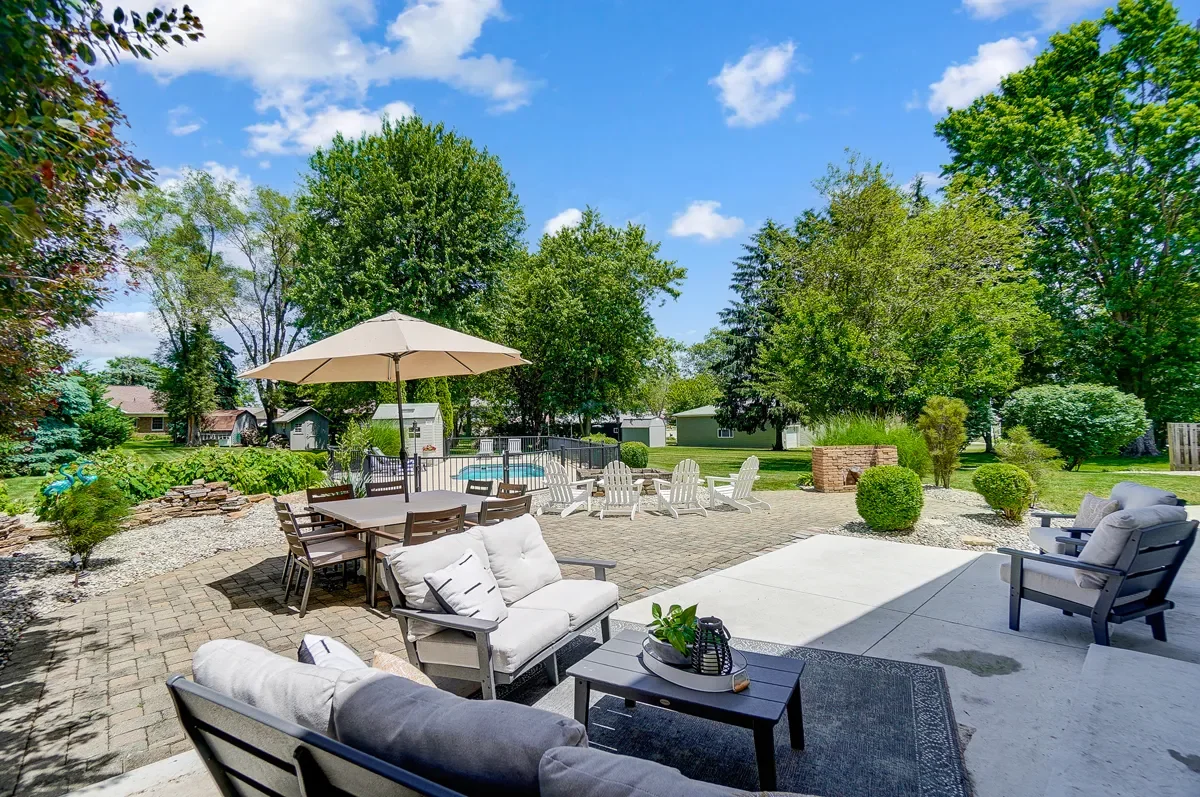 A backyard patio with outdoor furniture, including cushioned chairs, a dining table with an umbrella, and a seating area with Adirondack chairs.