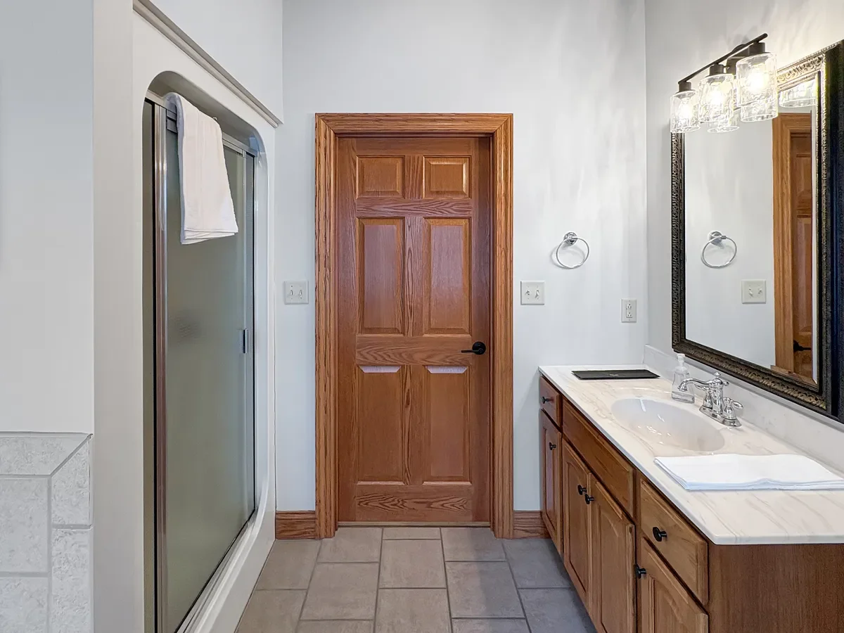 Bathroom with wooden door, mirror, sink, towel, and shower.