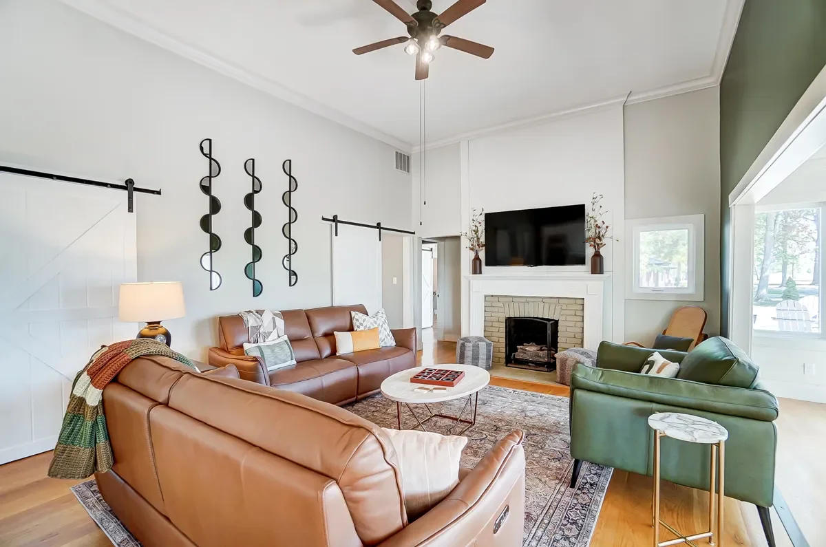 Living room with leather sofas, green armchair, fireplace with a mounted TV, decorative wall art, and a ceiling fan.
