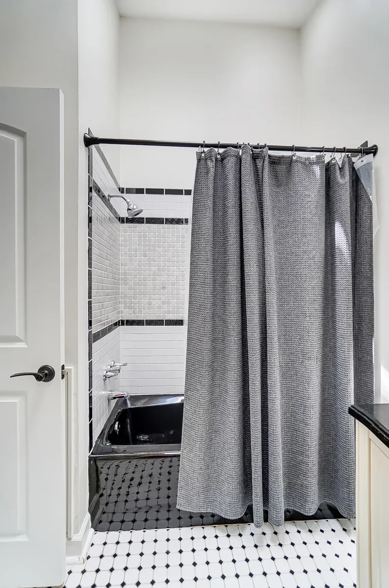 A bathroom shower stall with a black bathtub, gray shower curtain, and tiled walls in white and black.