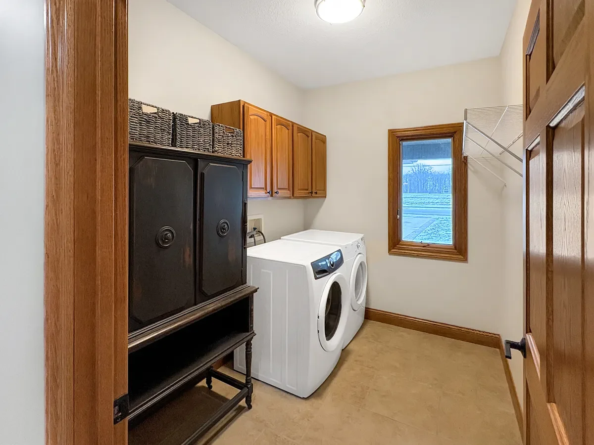 Laundry room with washing machine, wooden cabinets, window, and a wire shelf
