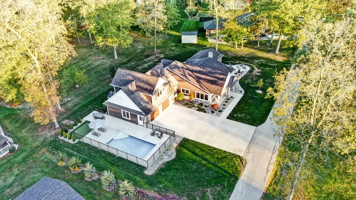 Aerial view of a residential property with a house, swimming pool, and patio area surrounded by trees and greenery.