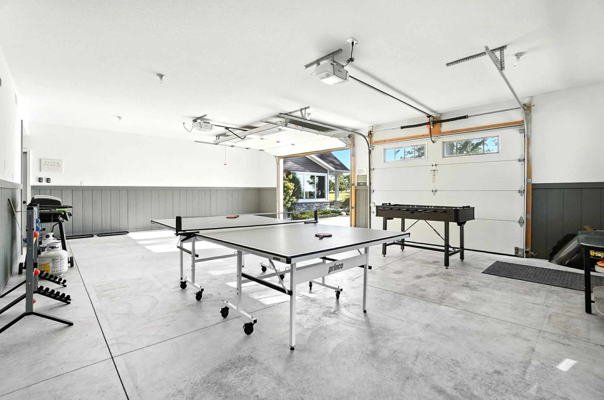 Indoor garage with ping pong table, foosball table, and yard games. Large open space with garage door open to outside.