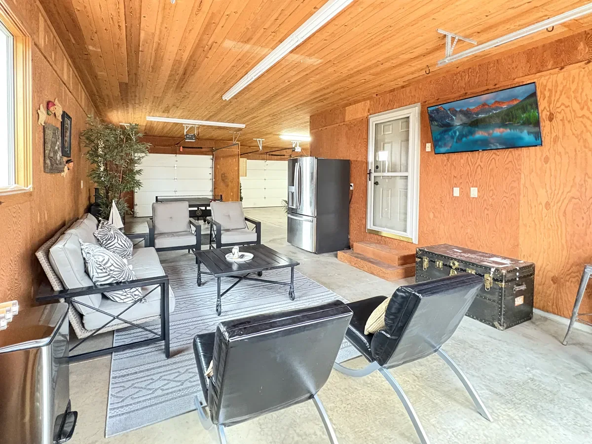Living room with wooden walls and ceiling, black and white furniture, a flat-screen TV on the wall, a metal trunk, and a garage door in the background.