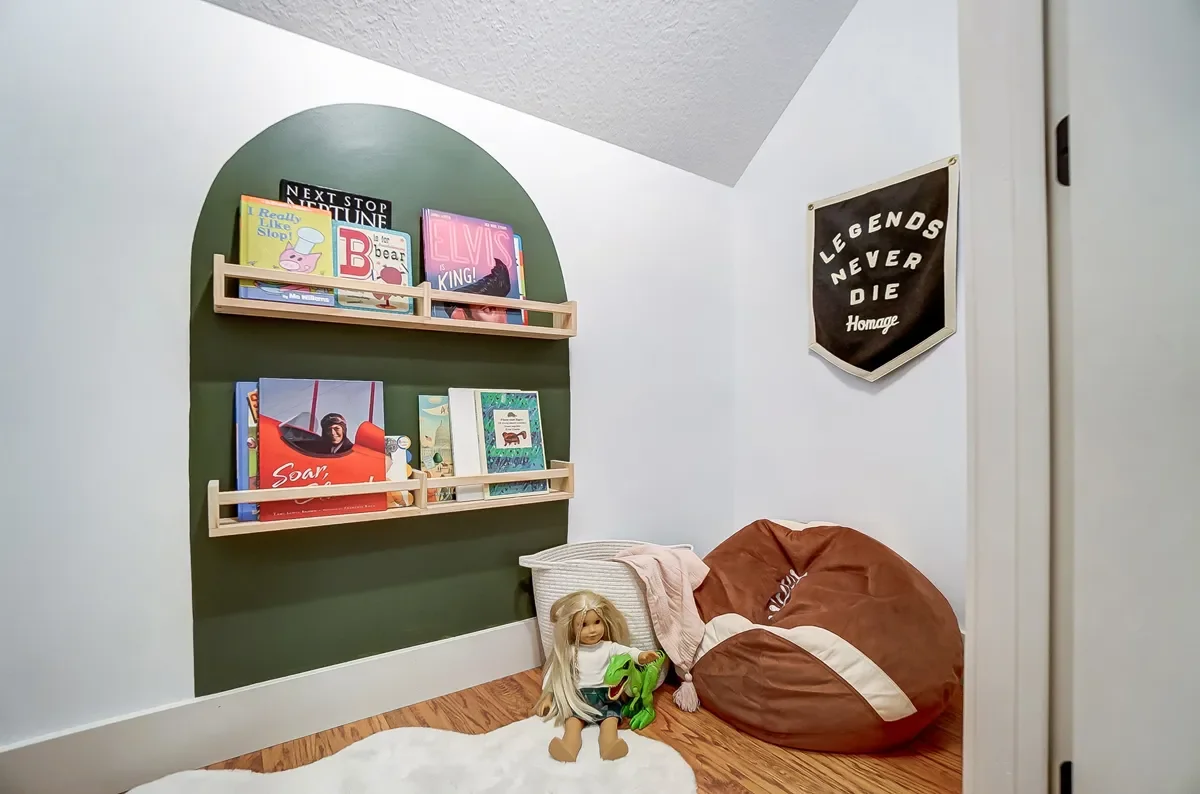 Corner of a child's bedroom with a green semi-circle wall shelf holding children's books, a 