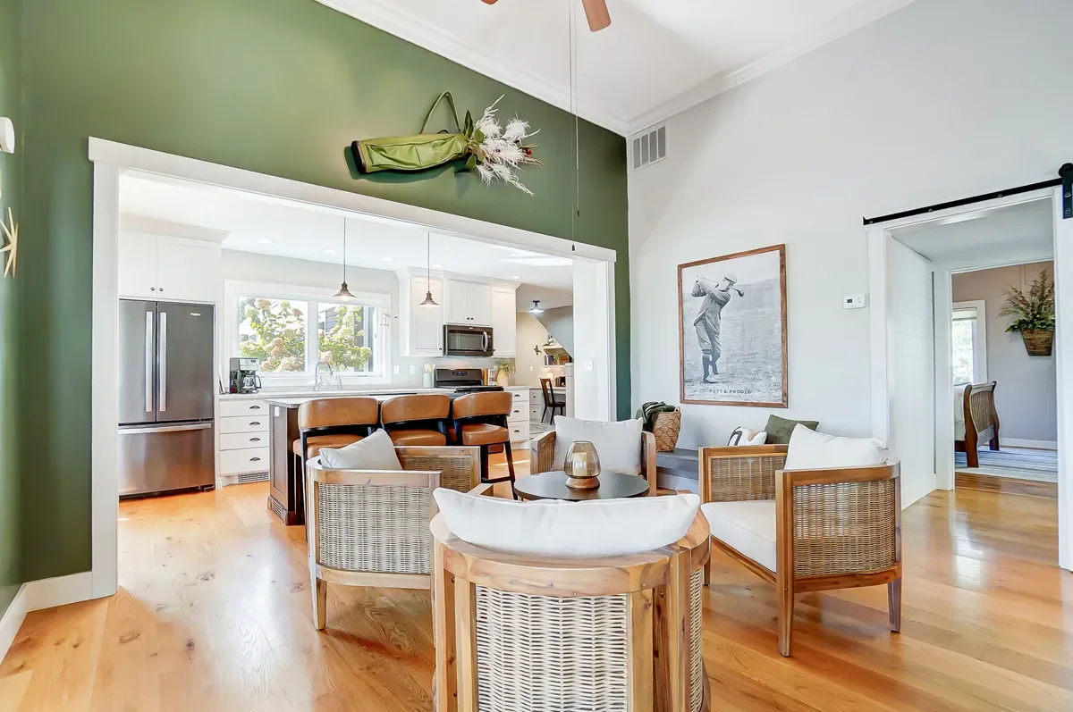 Open living room and kitchen with green and white walls, wooden furniture, and hardwood floors.