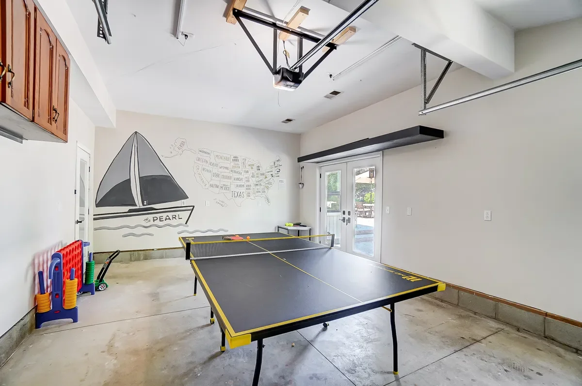 A garage converted into a game room with a ping pong table, wall mural of a sailboat and map of Texas, and a Connect Four game set. There are sliding glass doors leading outside.