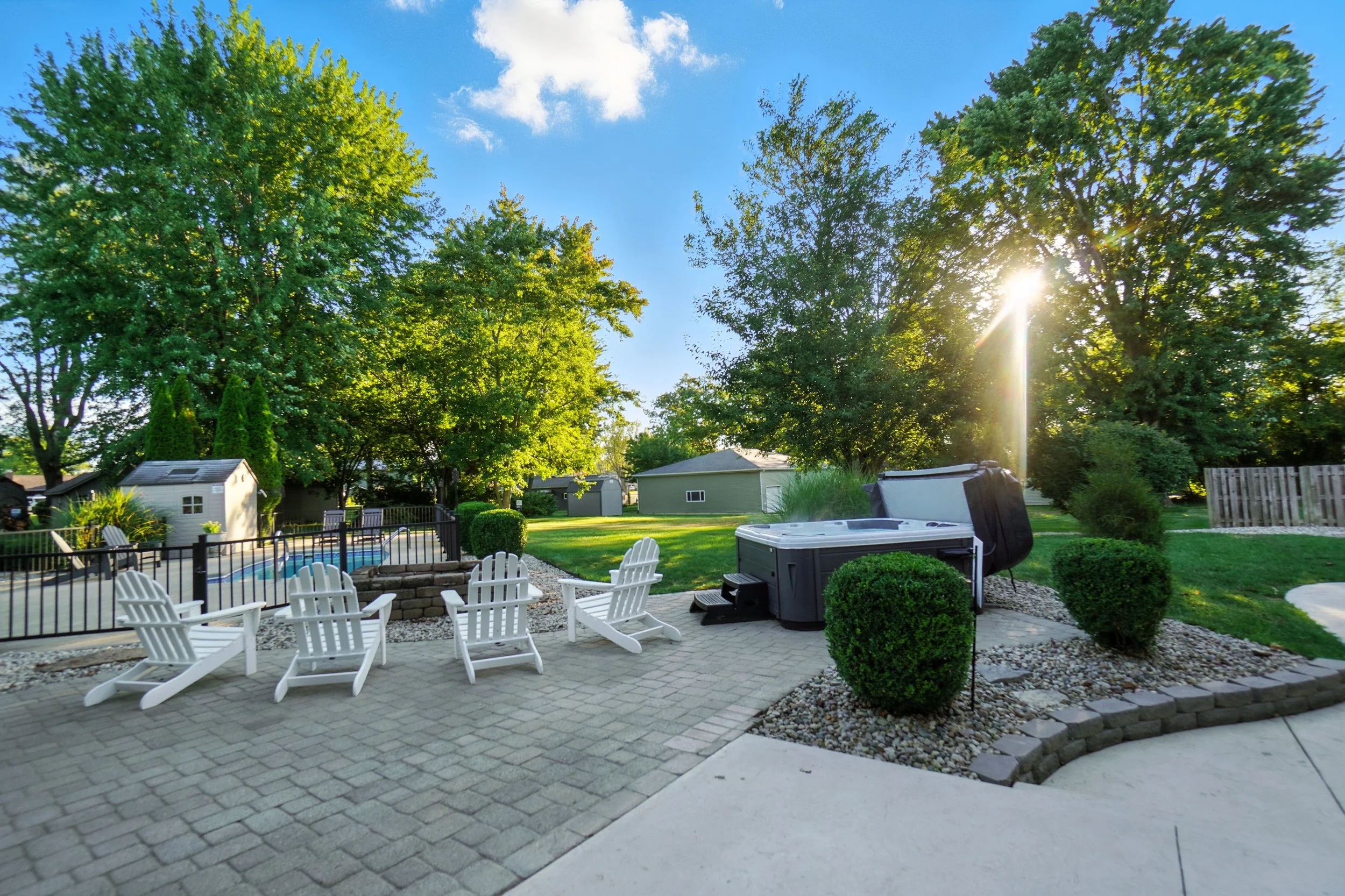 Backyard with patio, adirondack chairs, hot tub, swimming pool, trees, and a clear blue sky at sunset.
