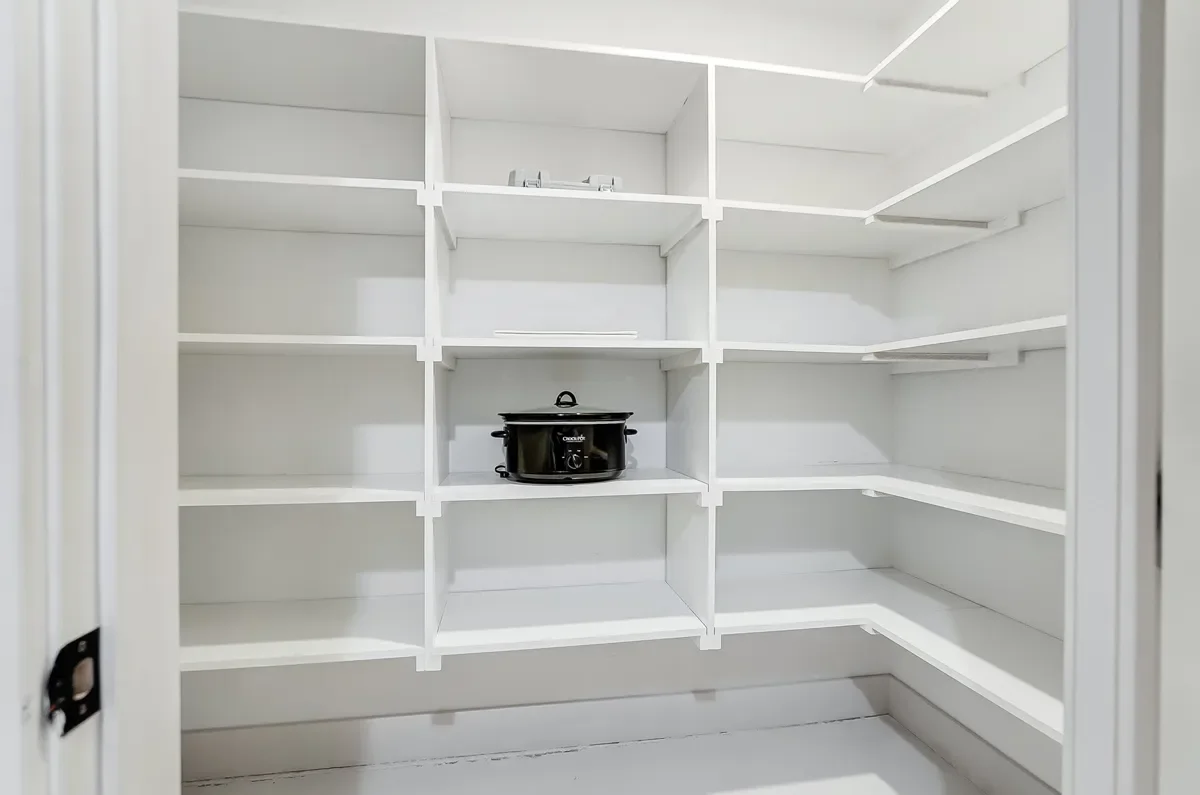 Empty white pantry cabinet with several shelves and a slow cooker on one shelf.