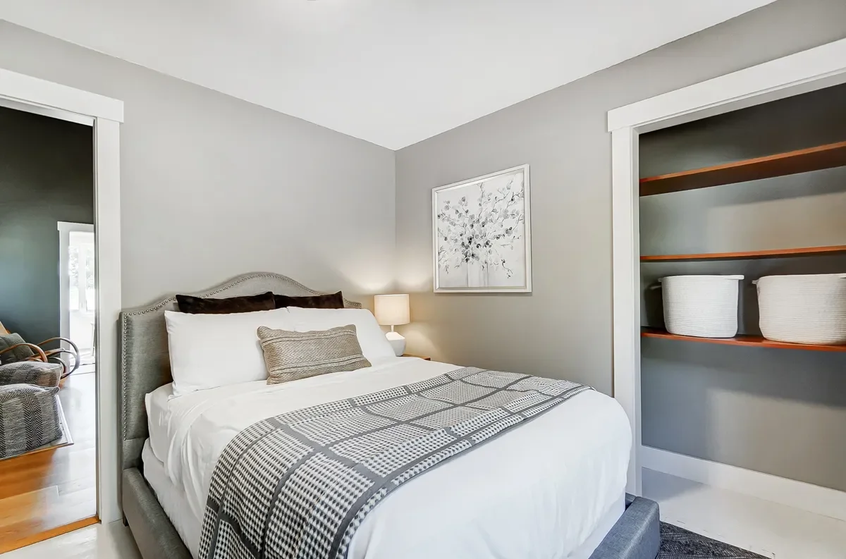 A bedroom with a bed, framed artwork, nightstand with lamp, and built-in shelves with baskets