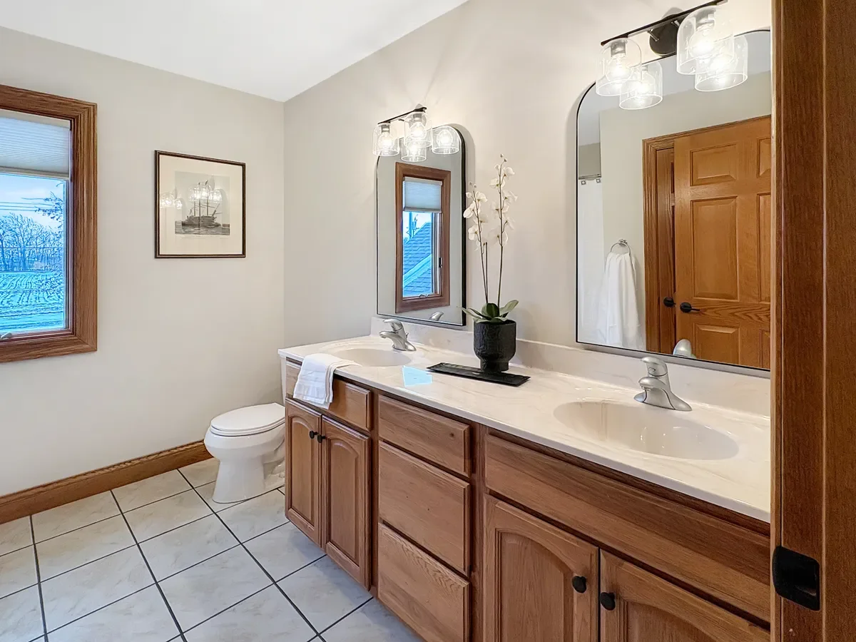 Bathroom with a double vanity, large mirror, potted orchid, towel, window, and wooden door.