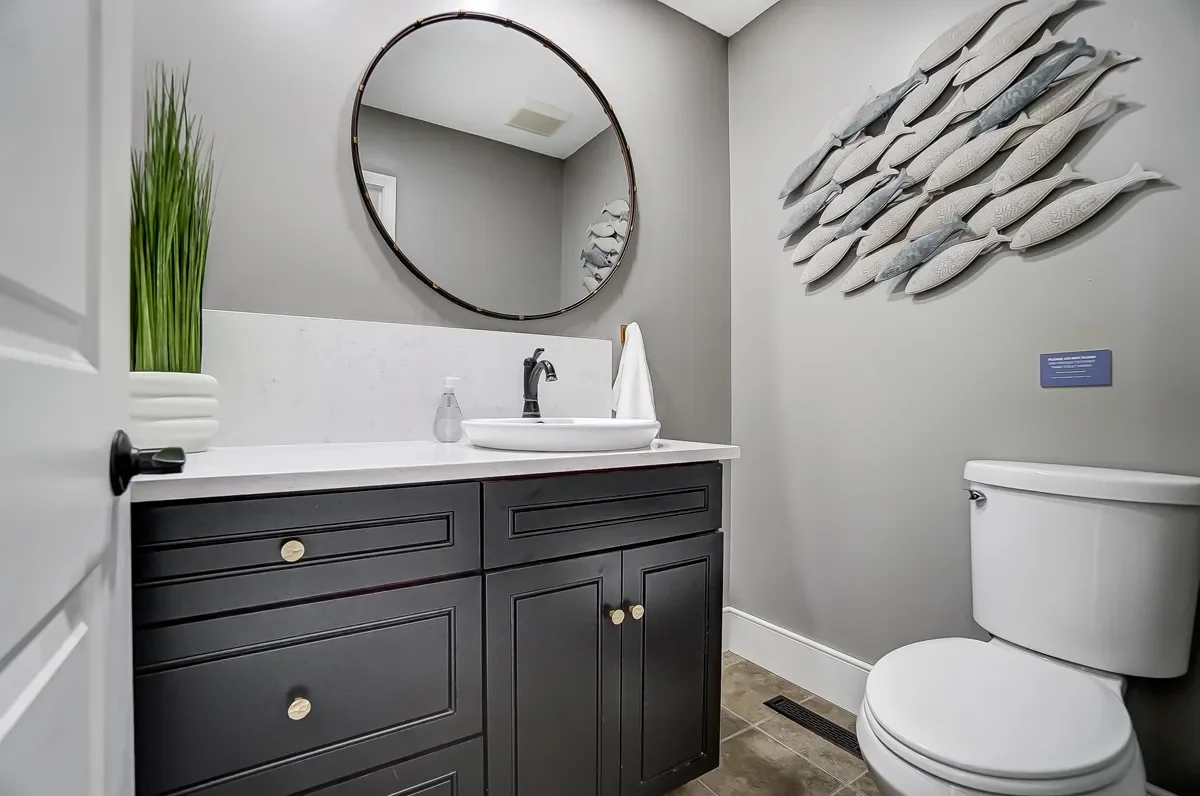 A modern bathroom with a white countertop and a black vanity, a round mirror, a potted plant, a fish wall sculpture, a soap dispenser, a towel, and a toilet.
