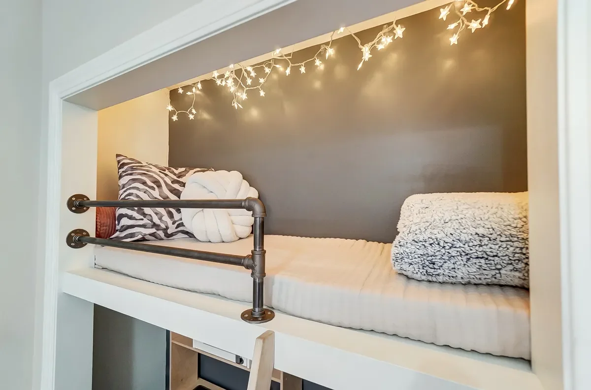 A cozy built-in bed nook with string lights, pillows, and blankets.