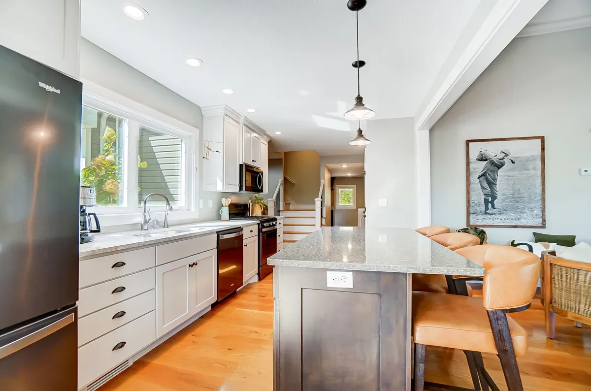 Modern kitchen with white cabinets, stainless steel appliances, granite countertops, a large island, and a dining area with leather chairs and wall art.