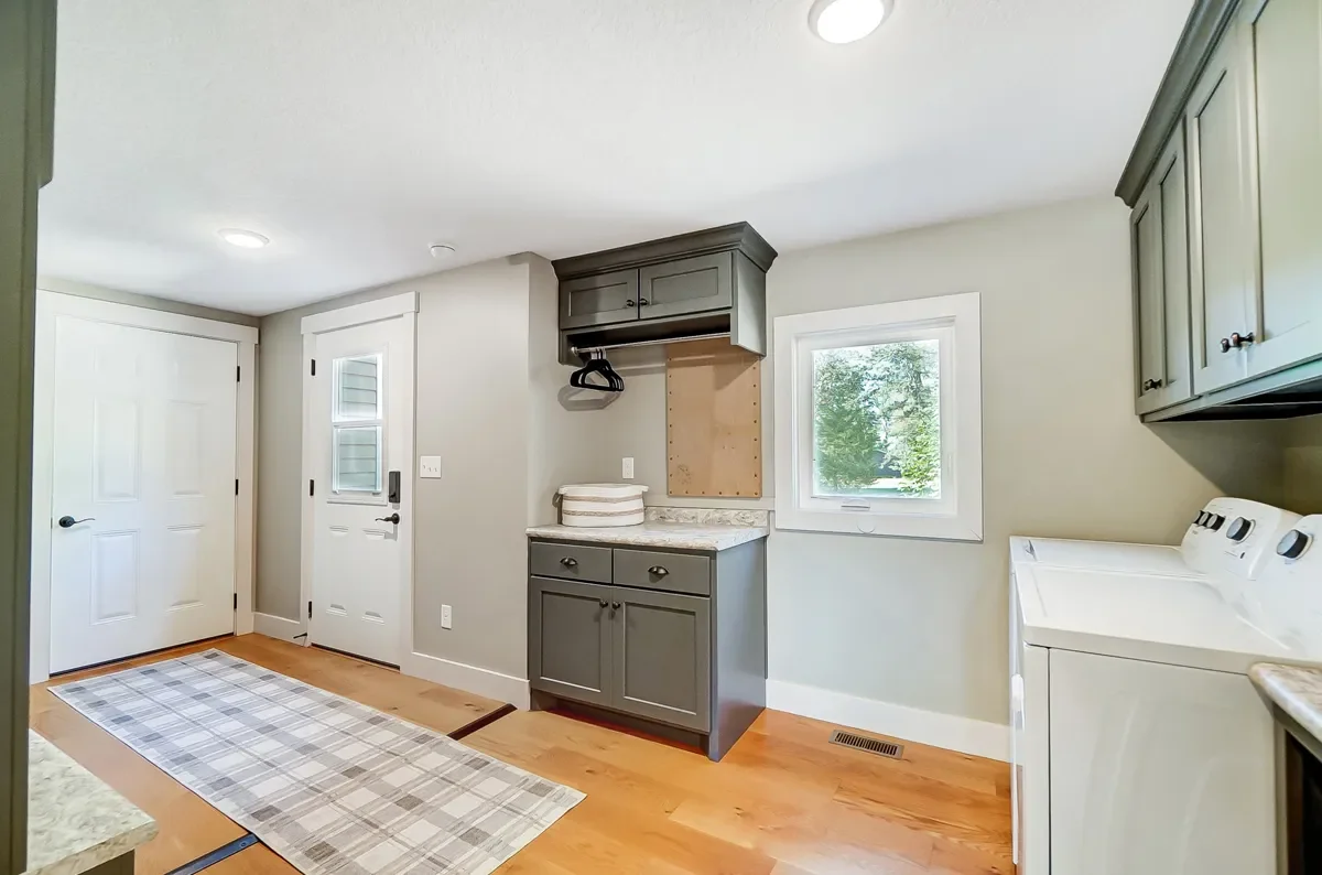 A laundry room with a white washing machine, gray cabinets, a small window, and a door leading outside.