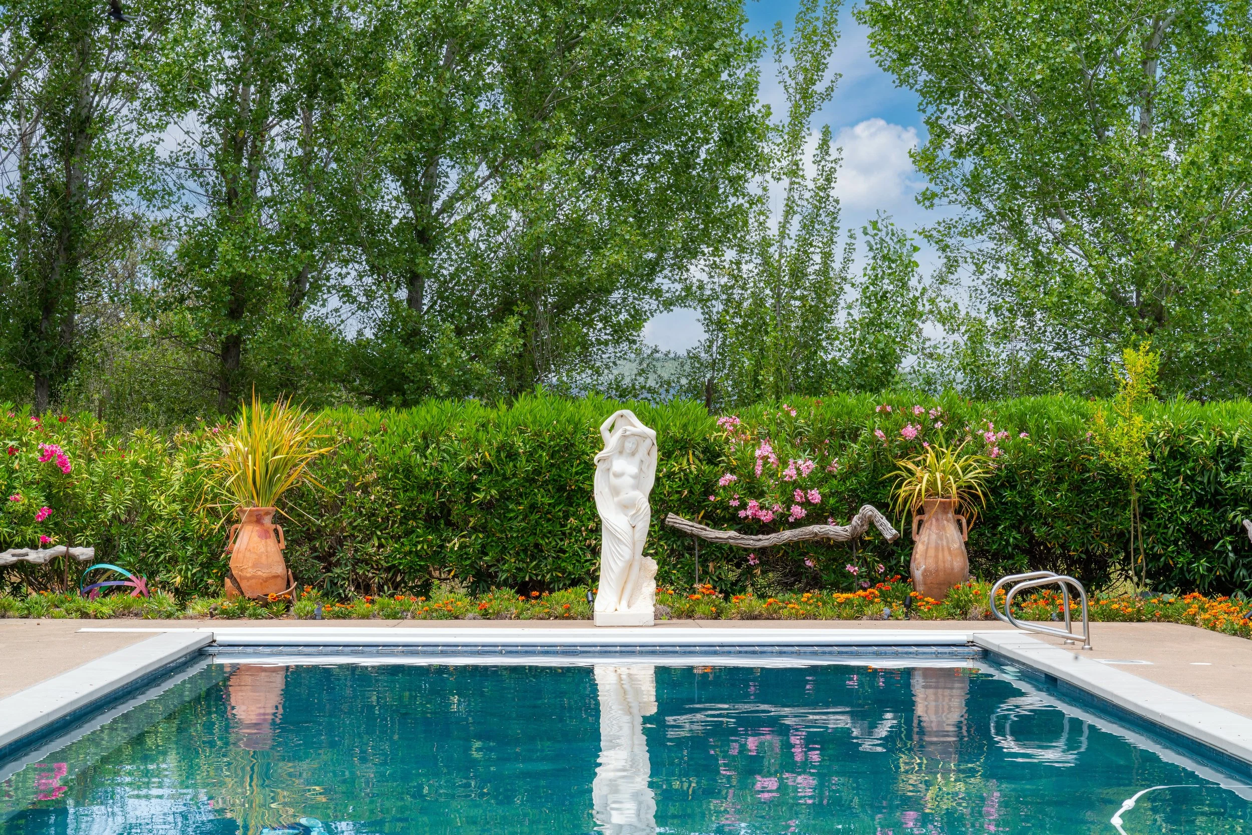 Swimming pool with statue of a woman and lush greenery in the background.