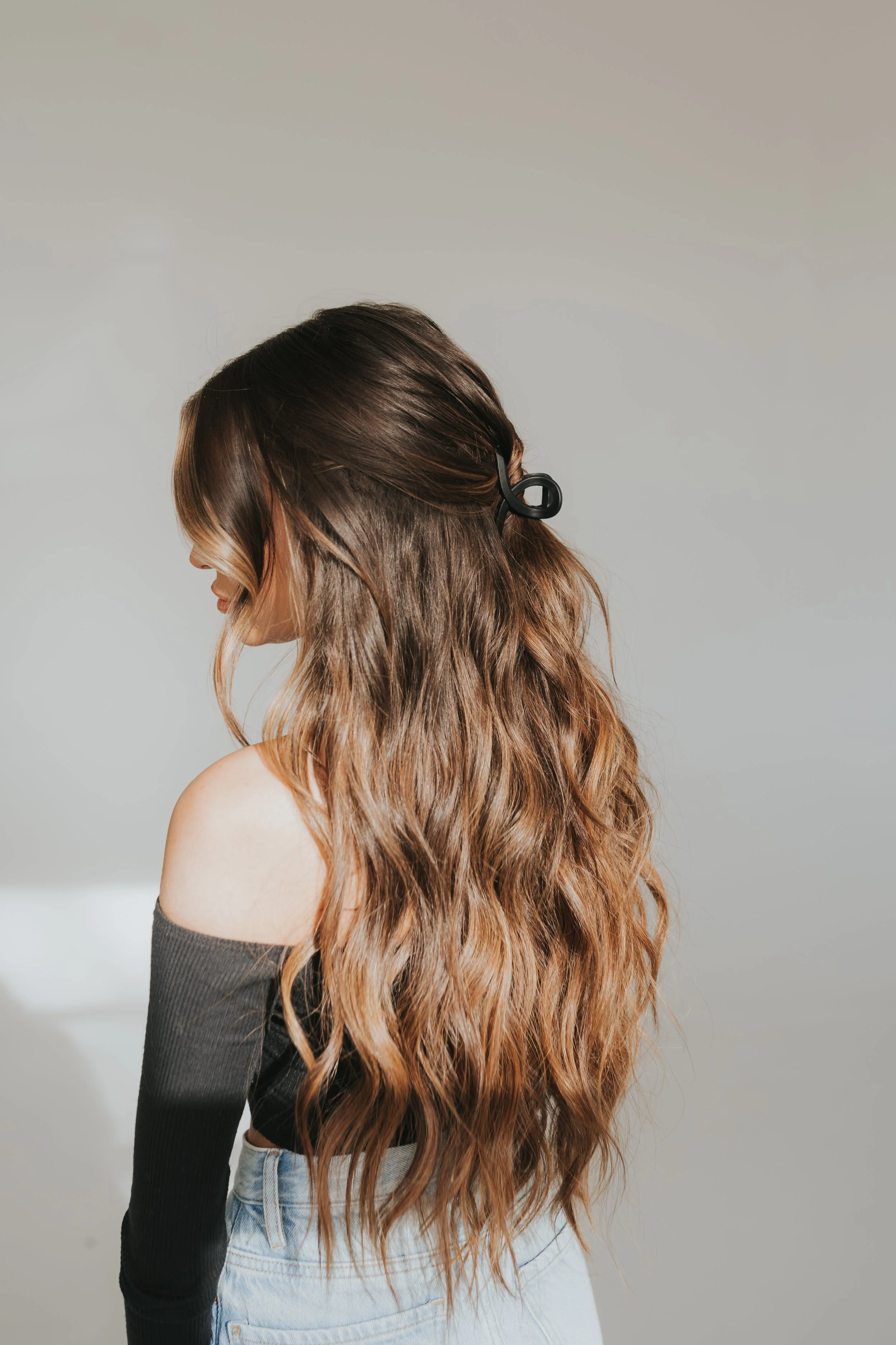 Long brown hair extensions with balayage hair color, half up in a claw clip.