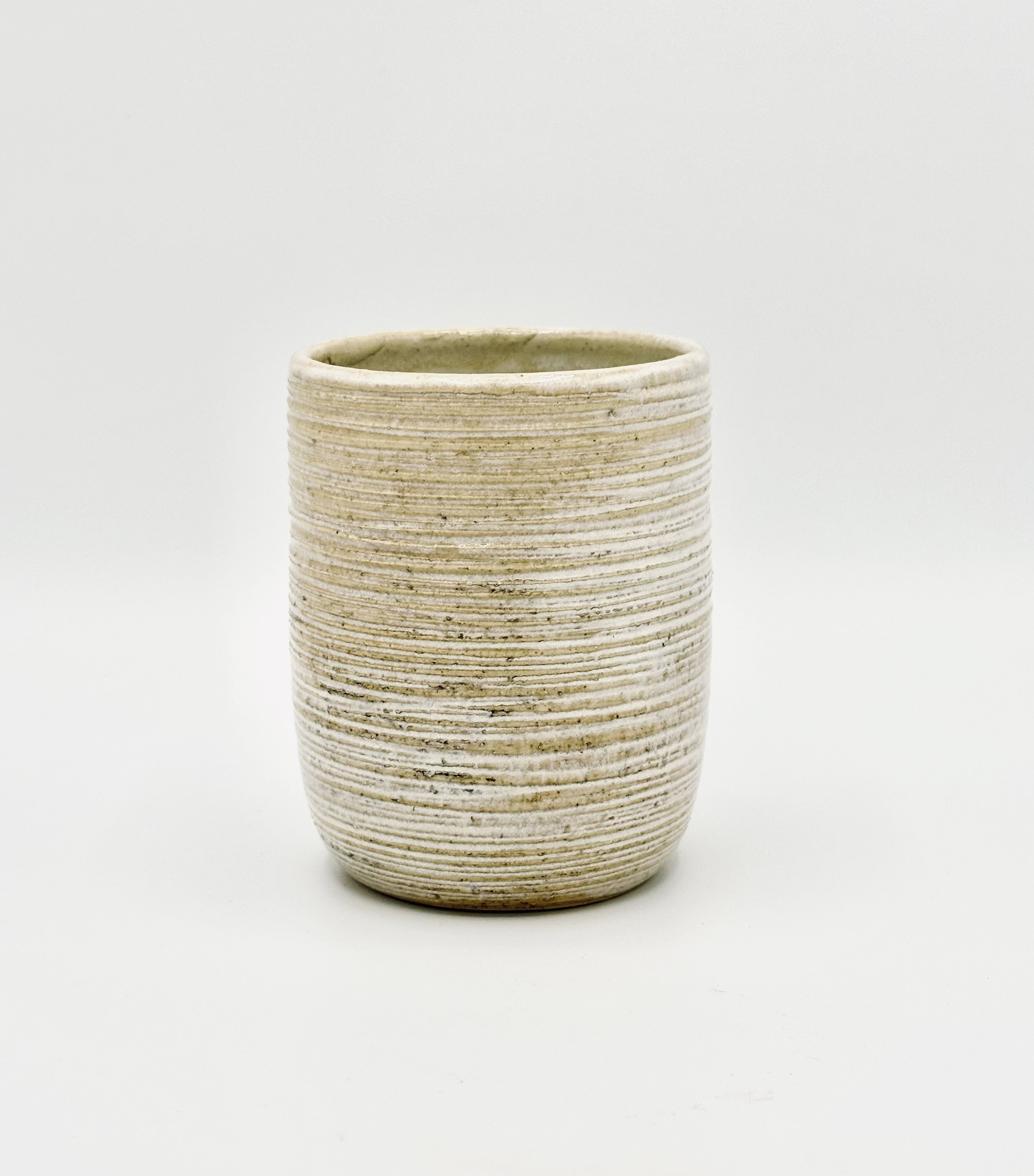 A beige ceramic pot with horizontal ridges on a white background.
