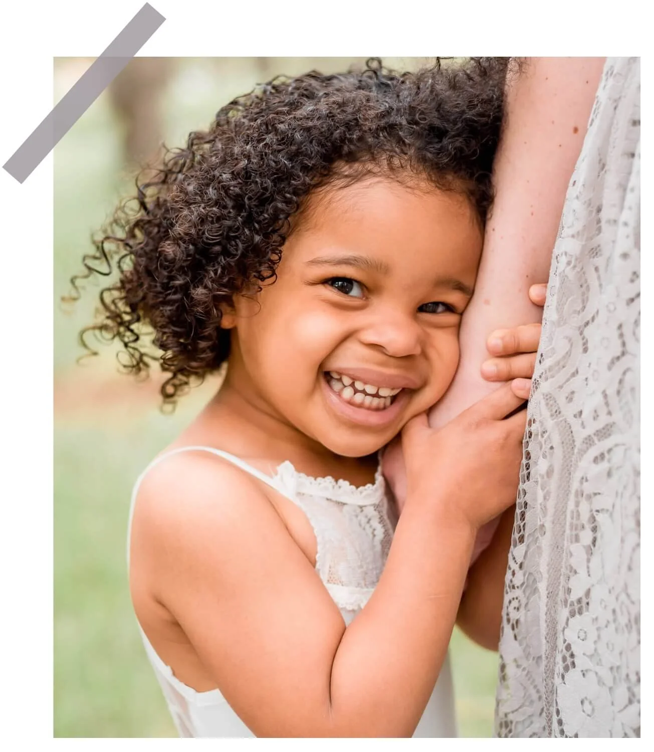 little girl holding onto her moms arm smiling at camera