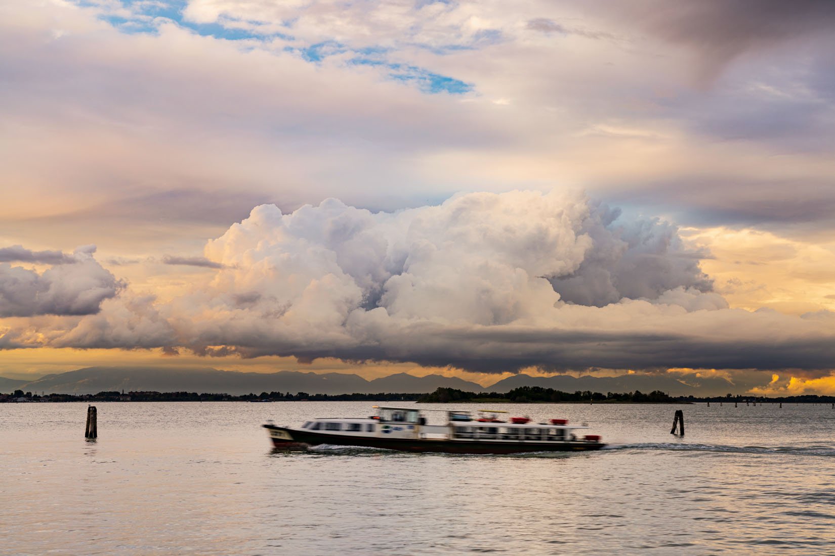 A vaporetto (waterbus) in the lagoon among pink and orange sunset clouds | Il vaporetto in laguna è immerso nelle nuvole colorate del crepuscolo