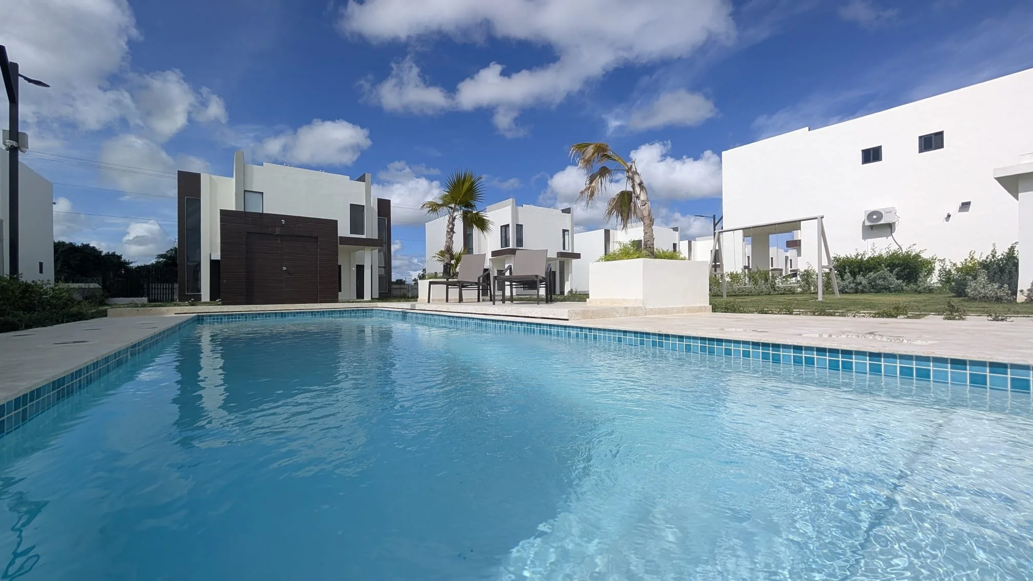 Modern houses with a swimming pool, palm trees, and a blue sky with clouds
