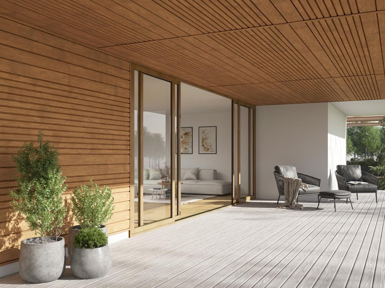 Modern outdoor balcony with wooden ceiling and wall, two potted green plants, two black lounge chairs with matching ottoman, and glass sliding doors leading to an indoor living room.