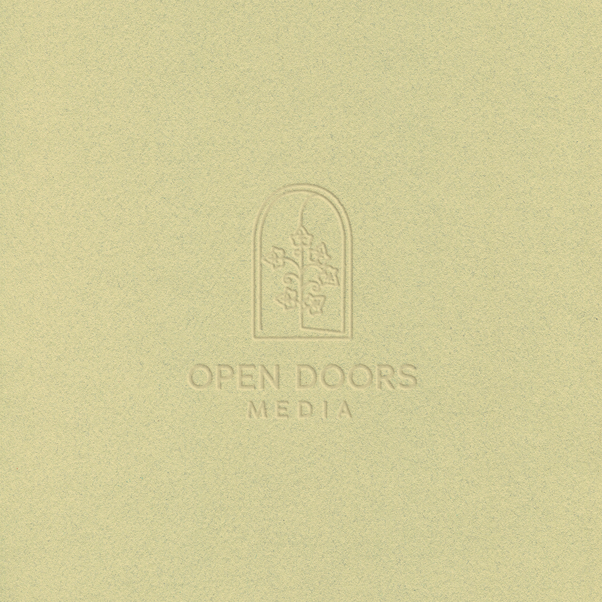 Mockup of Open Doors media logo embossed on light green paper; logo has an arched door with intertwined ivy leaves and the words "Open Doors Media" below.