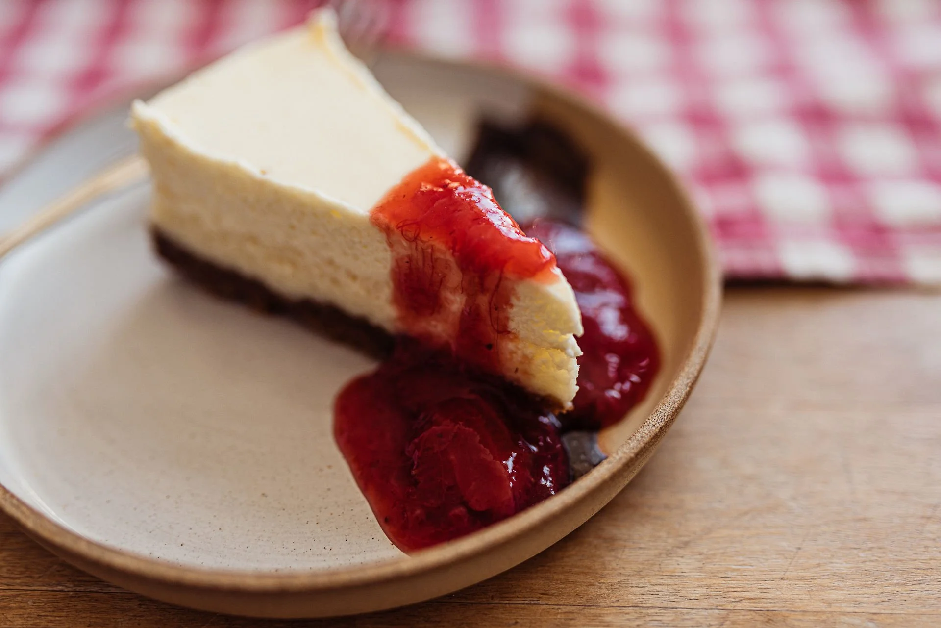 A slice of cheesecake on a ceramic plate with a red fruit sauce