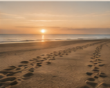 Sunset over the beach with footprints in the sand.