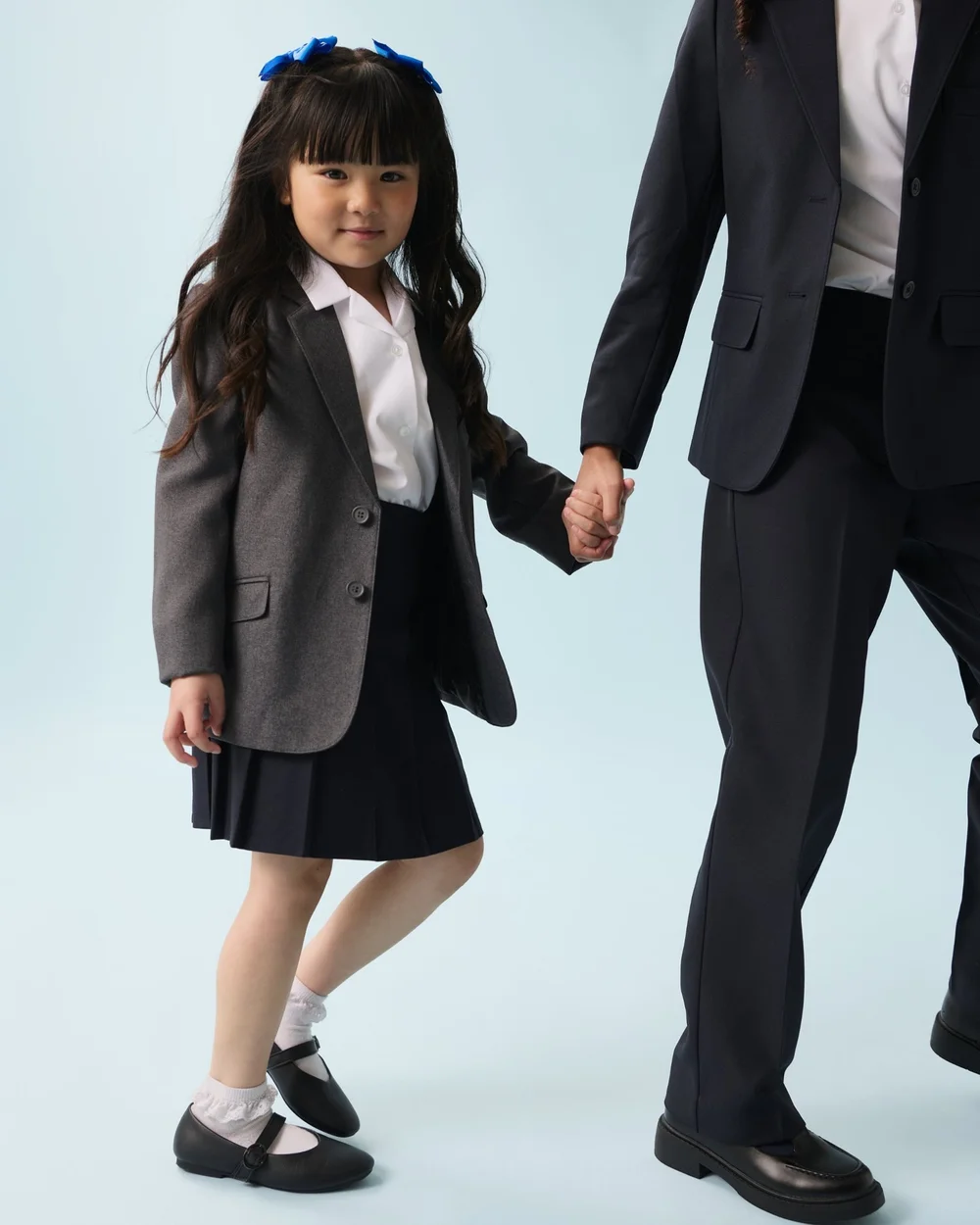 A young pupil in a grey blazer, white blouse and navy pleated skirt holding hands with an older pupil in a navy blazer and trousers