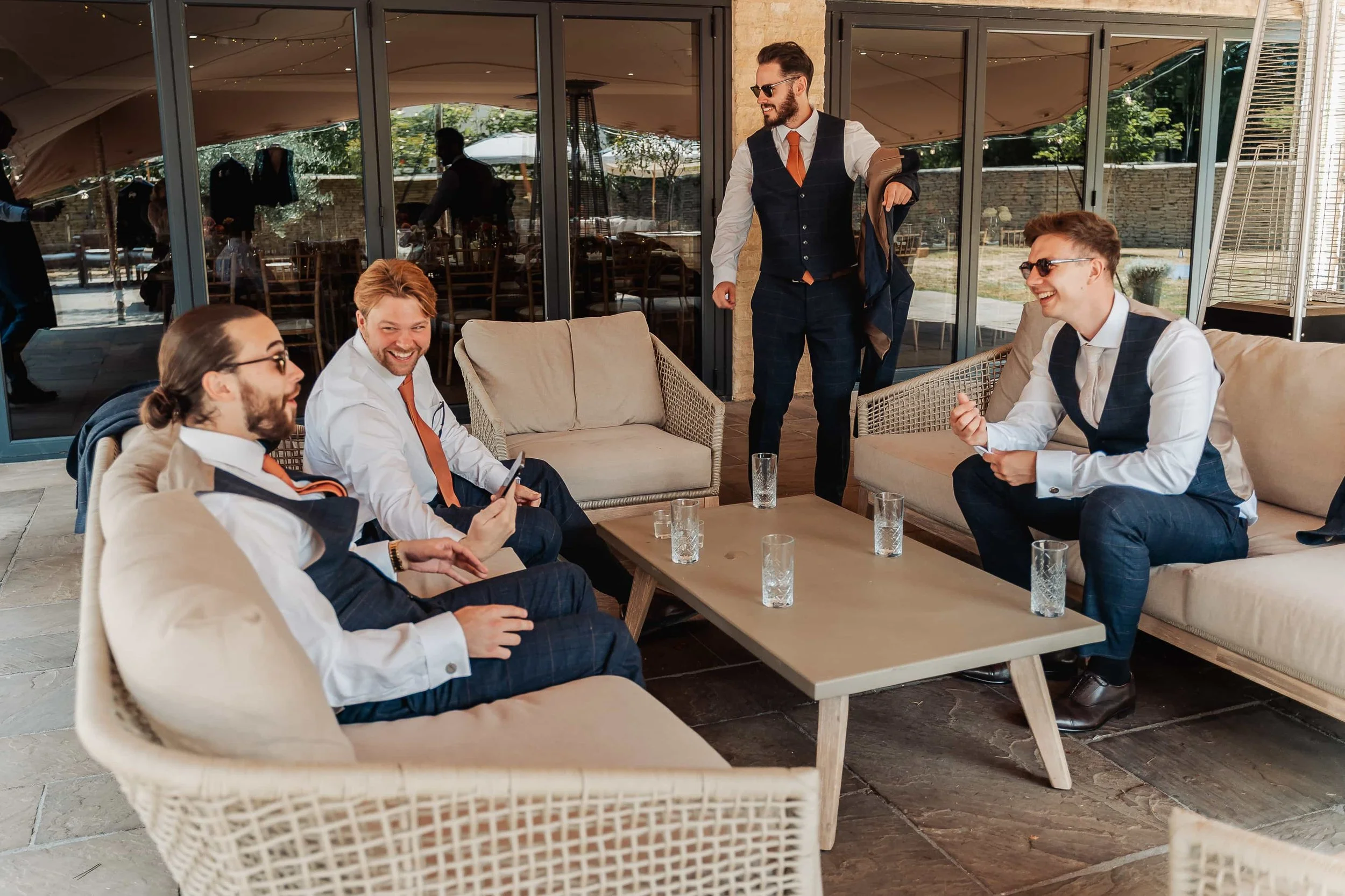Groomsmen relaxing on outdoor sofas at The Waters Edge at Ewen wedding venue in the Cotswolds