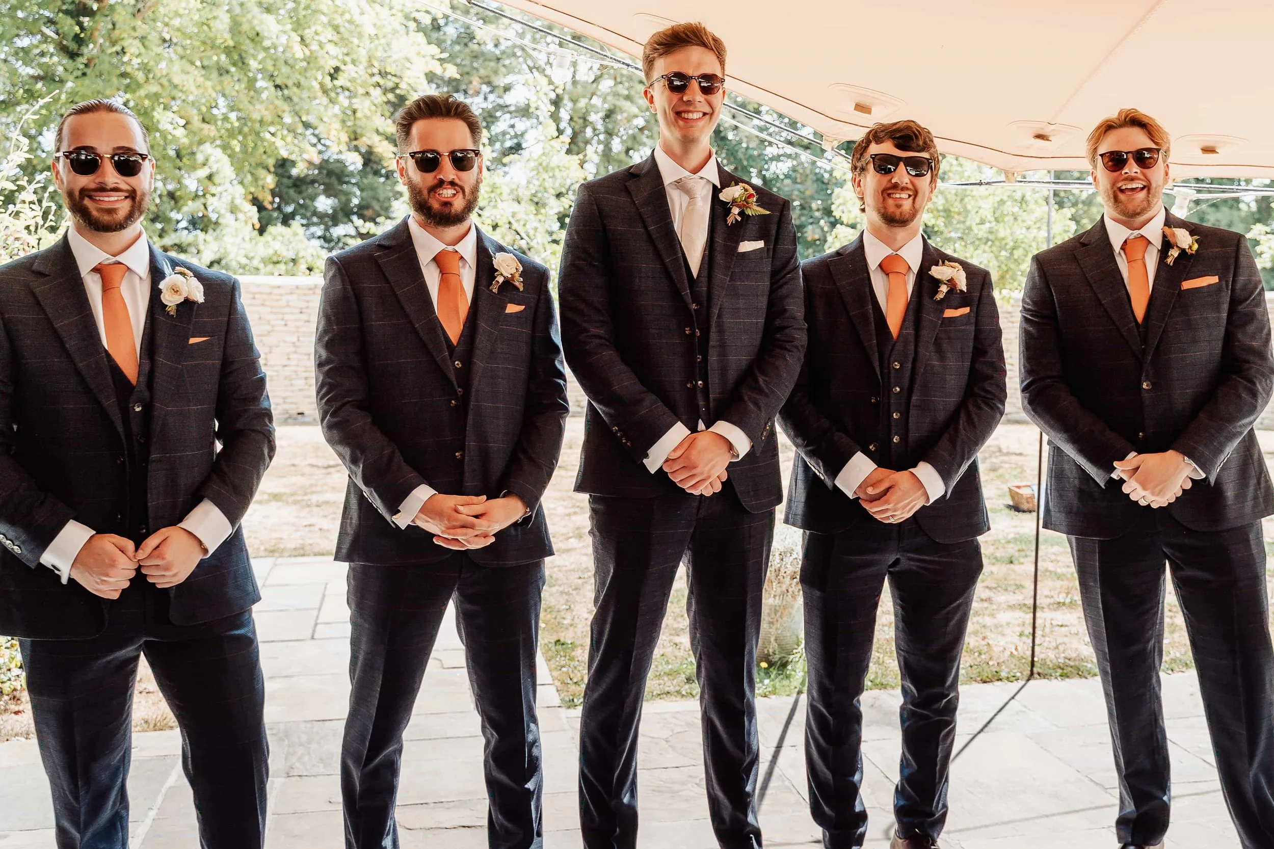 Groomsmen in matching suits and sunglasses lined up at a Cotswolds wedding