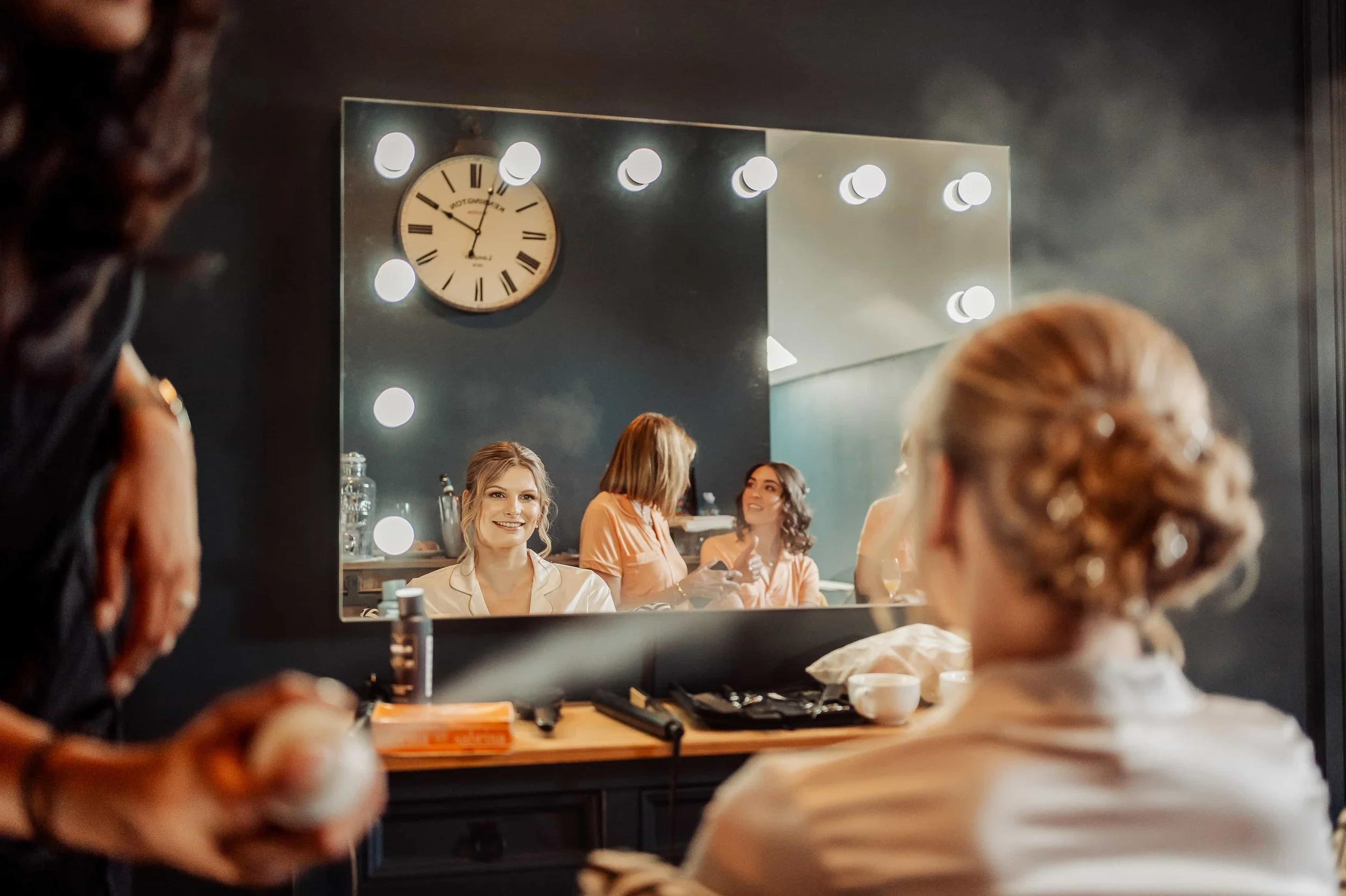 Bride reflected in a vintage mirror with bridesmaids getting ready in the background