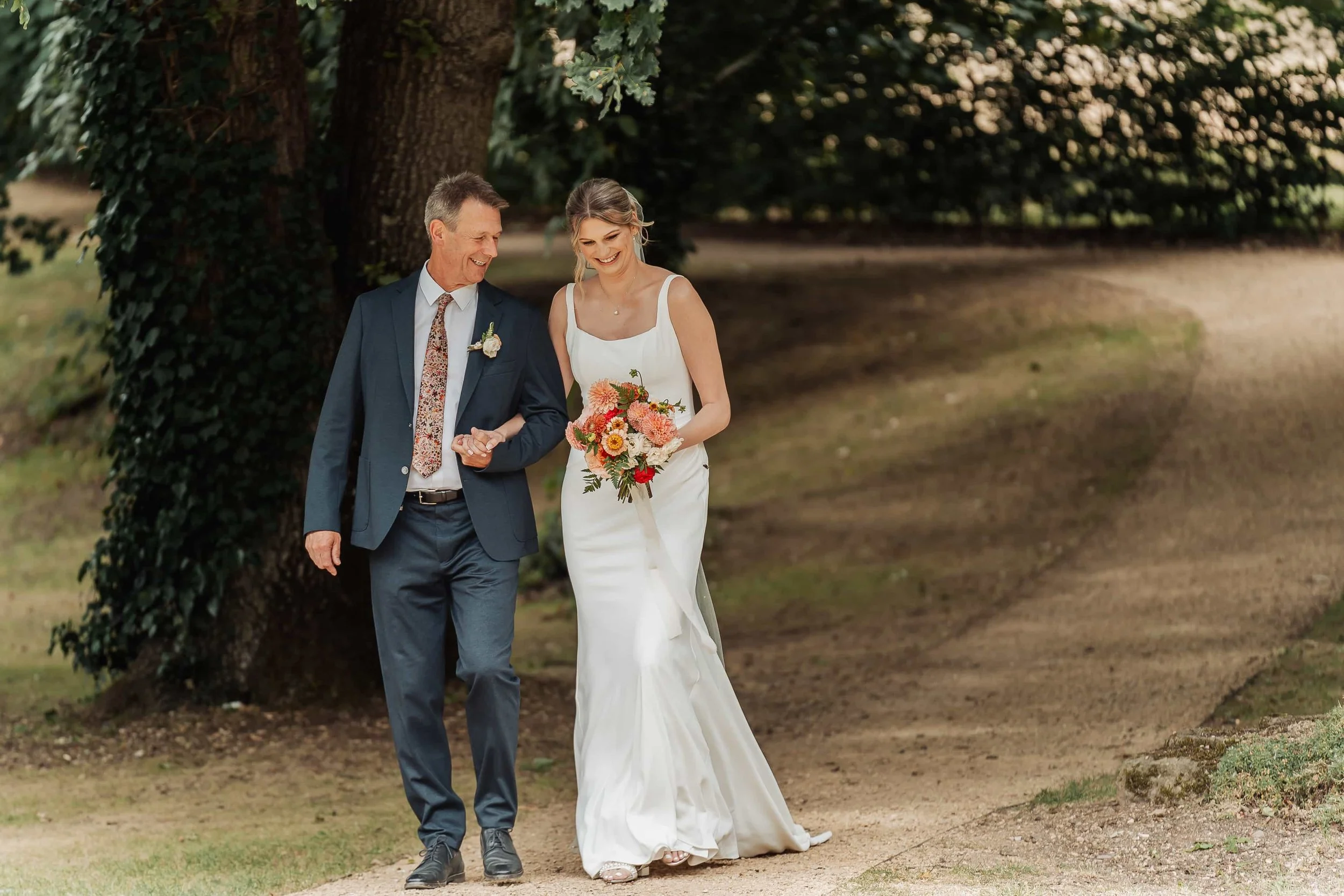 Father walking his daughter to her wedding ceremony under mature trees