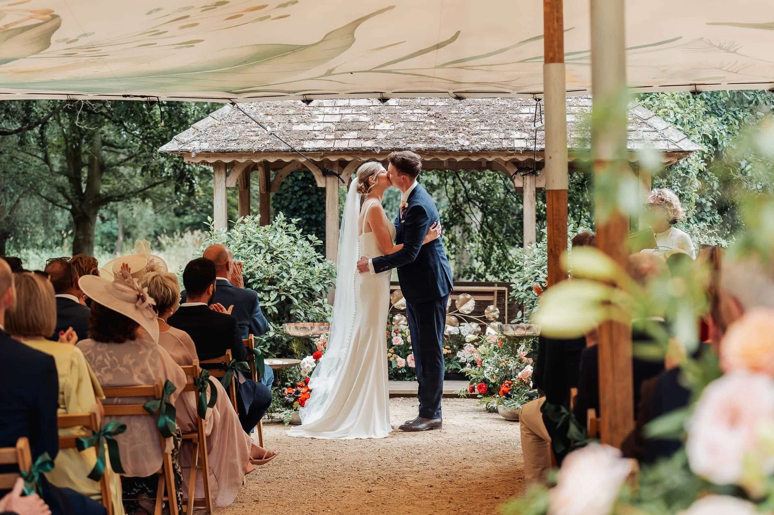 Bride and groom share their first kiss as a married couple under a garden gazebo
