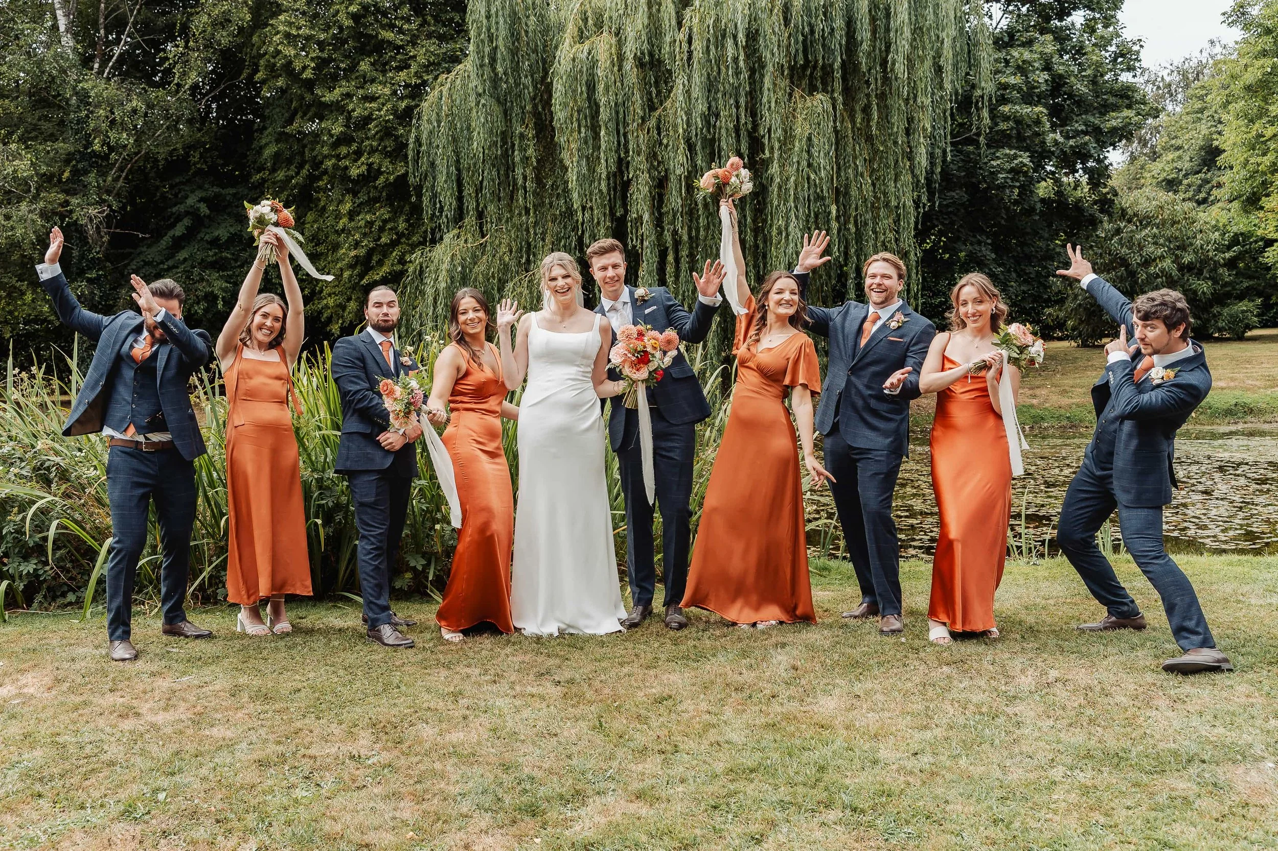 Wedding party jumping and celebrating with a weeping willow tree in the background
