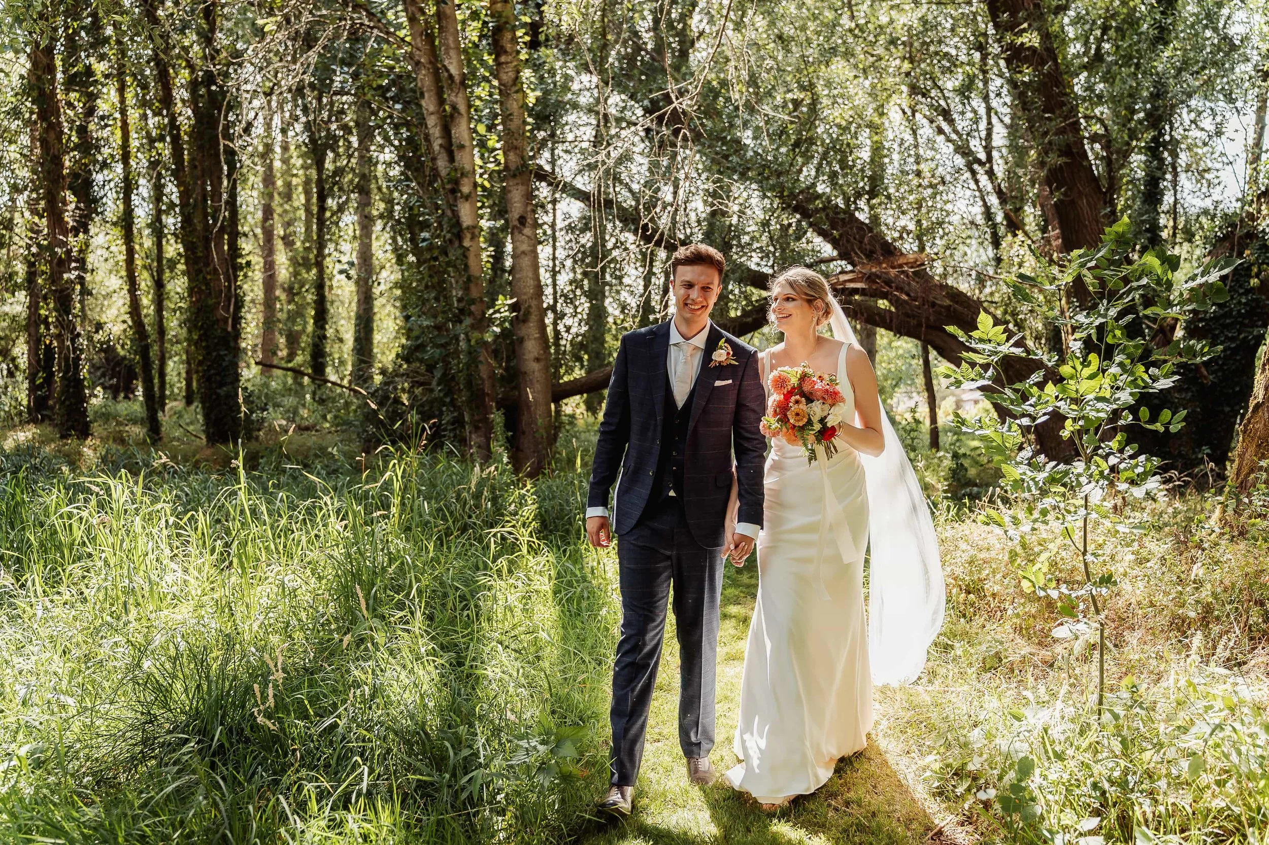 Bride and groom walking hand in hand along a sunlit woodland path