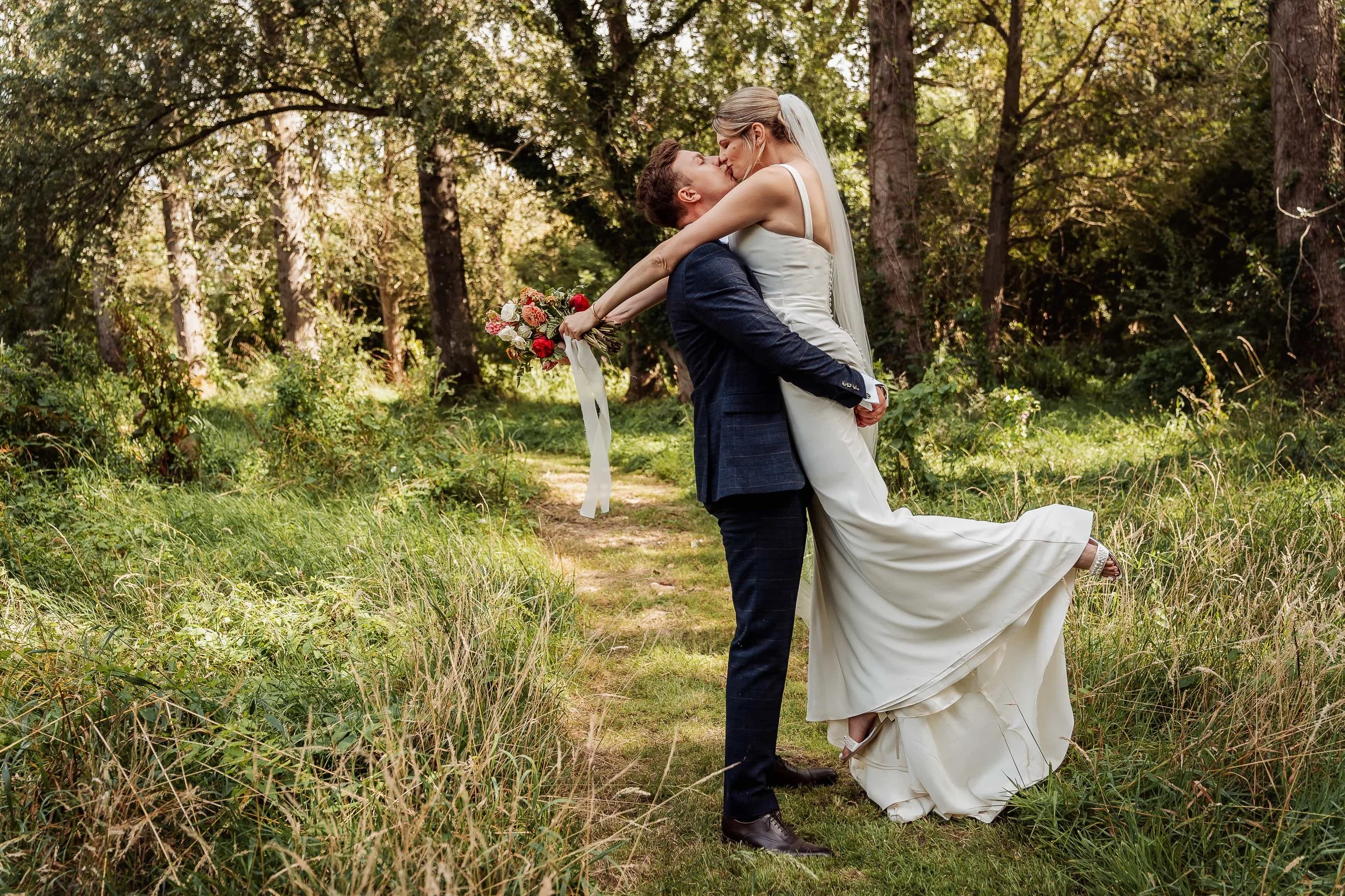 Groom dips bride for a kiss during golden-hour wedding portraits in the woods