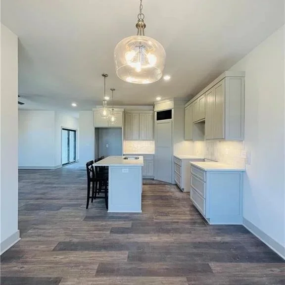 Empty kitchen with white cabinets, an island with chairs, and hardwood floors.