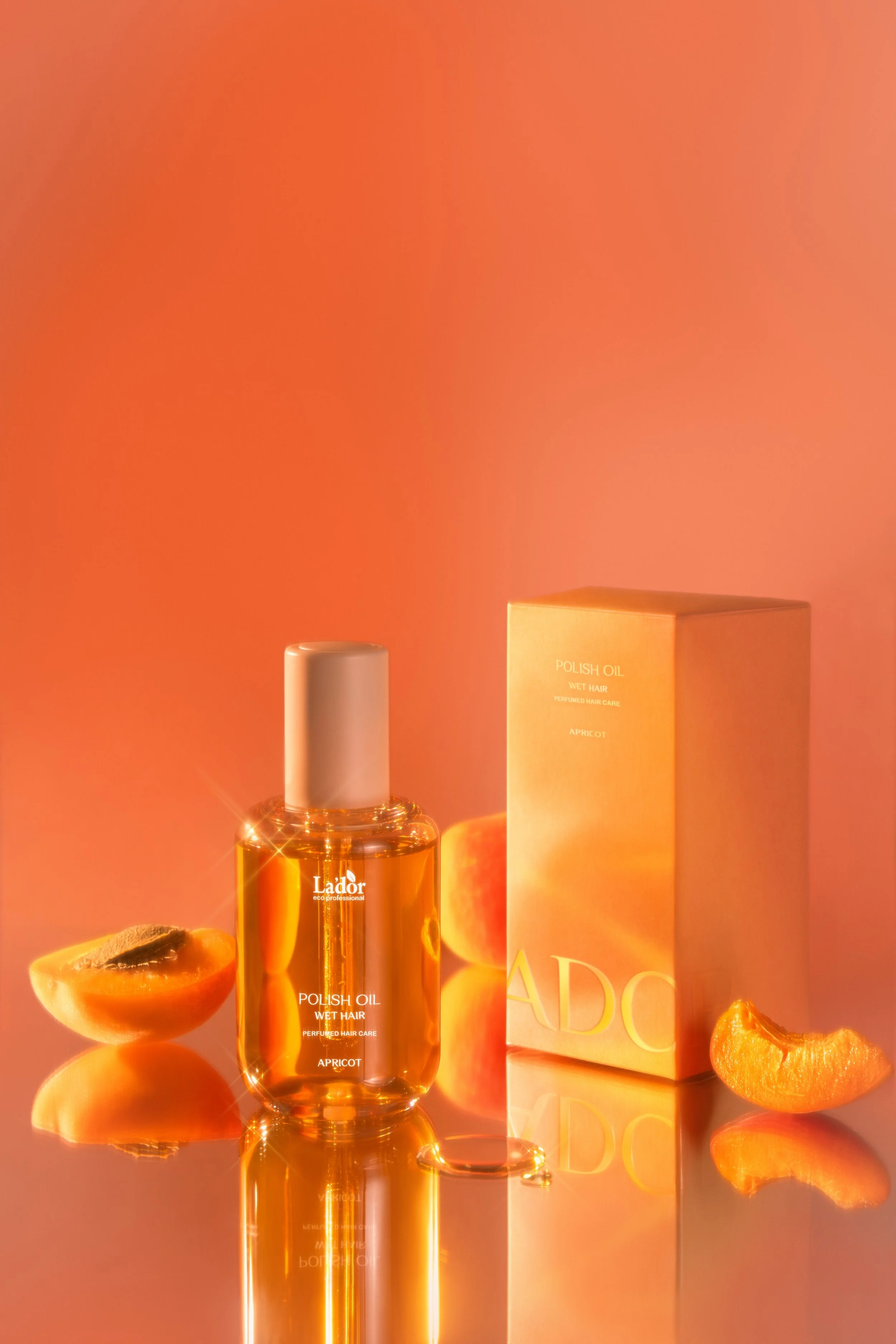 Bottle of apricot polish oil for wet hair next to a box and assorted apricot slices on a reflective surface with a warm orange background.