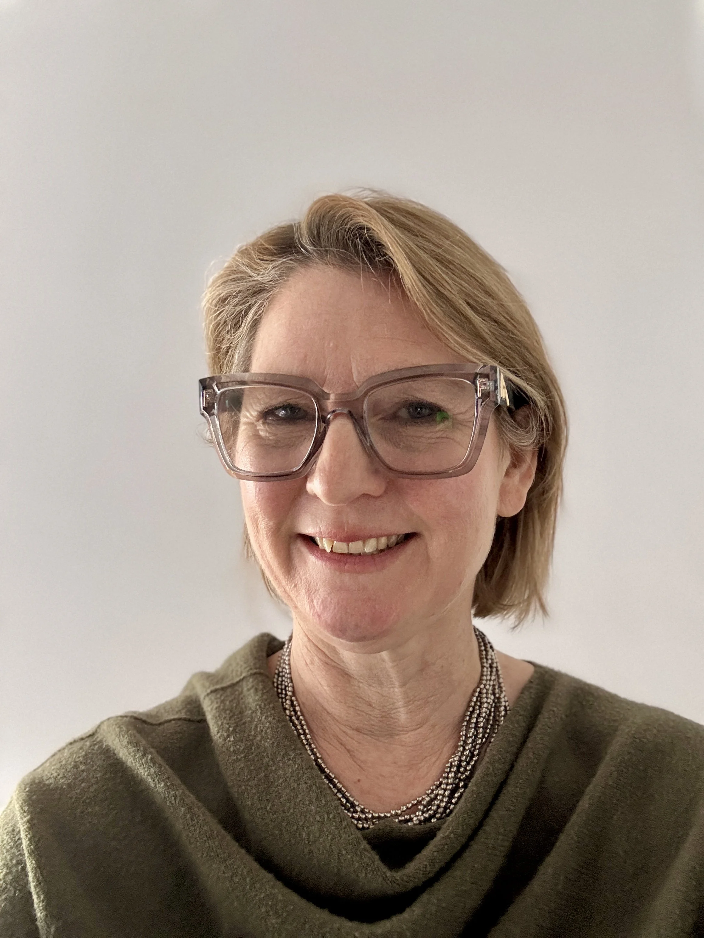 Dr Anna Baker smiling with grey glasses, wearing a green top and straight blonde hair to shoulder length