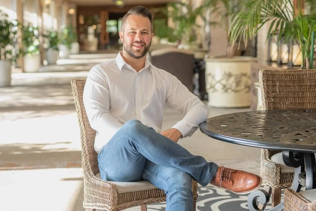 Man with beard sits in an outdoor courtyard