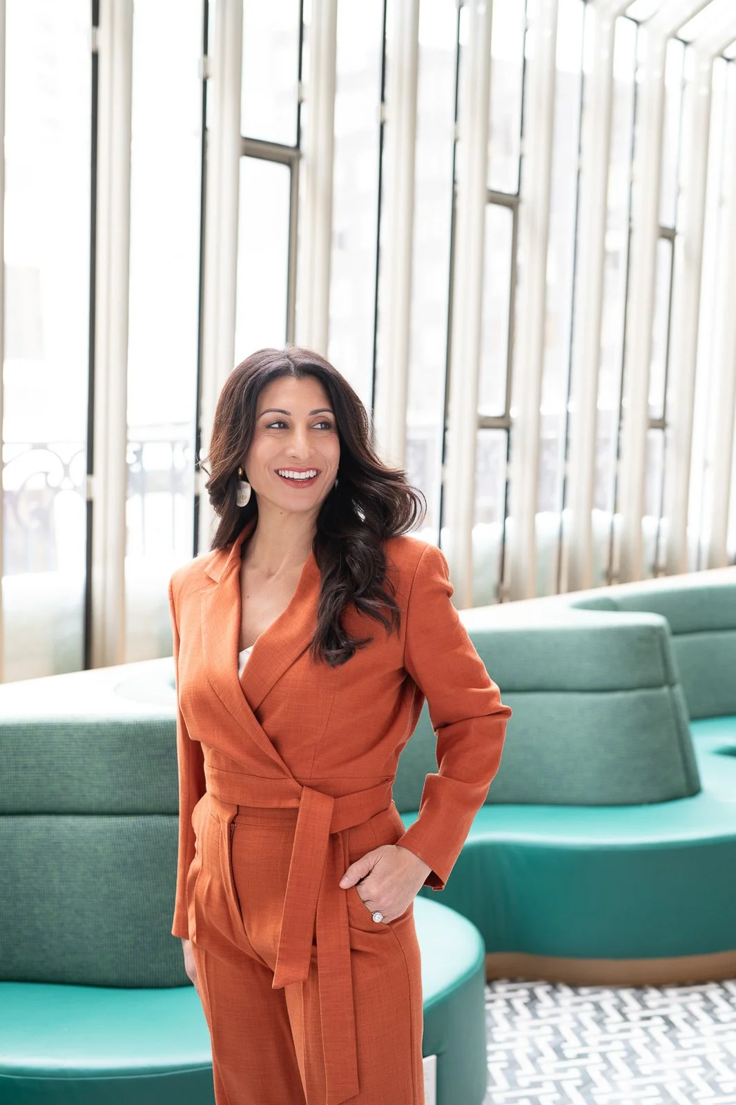 Professional woman in orange suit standing in architectural interior during executive branding photo shoot.
