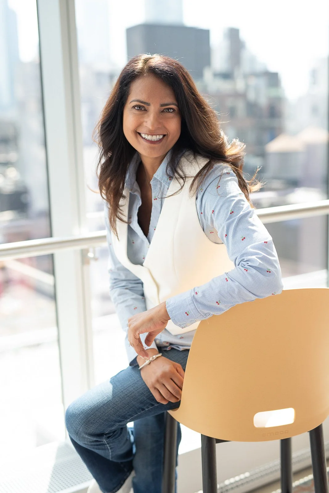 Professional headshot of female executive seated by window with city view — corporate portrait NYC