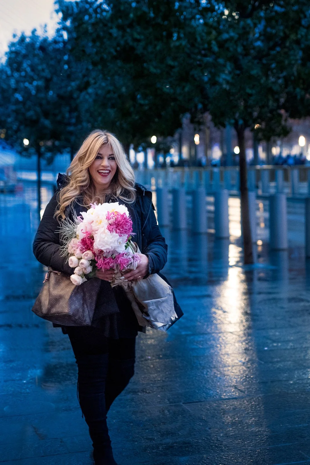 Proud florist walks down a rainy city street holding flowers