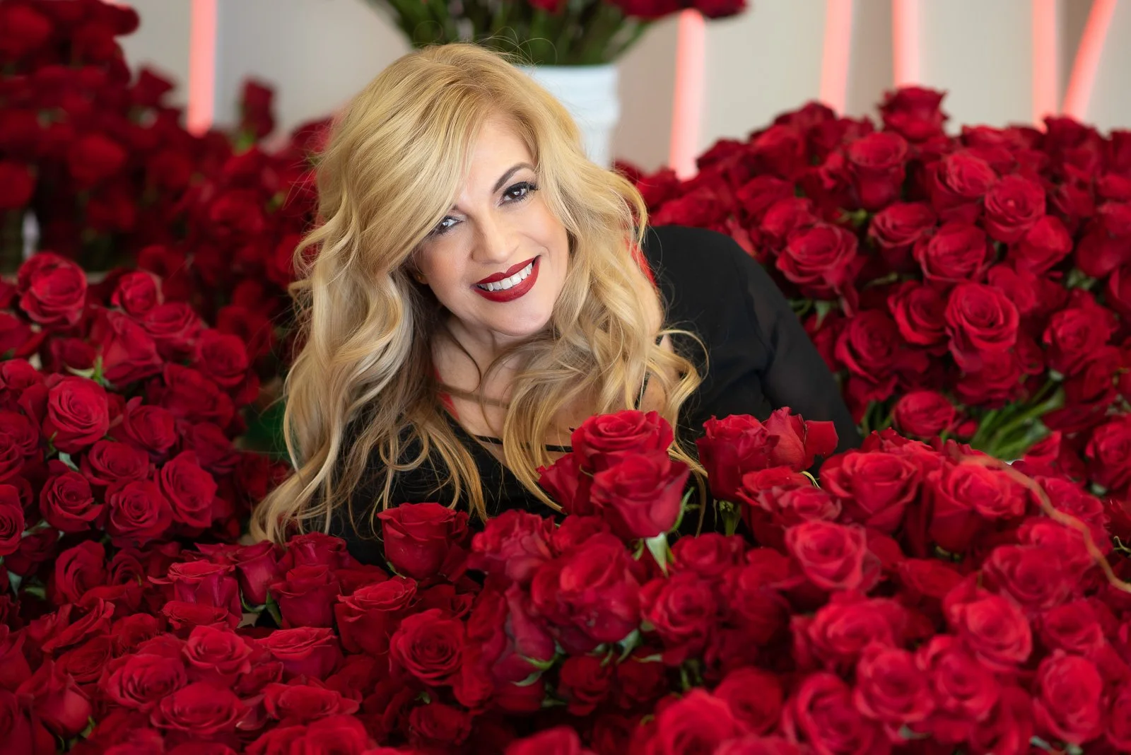 Blonde entrepreneur surrounded by red roses during creative editorial branding photography shoot.