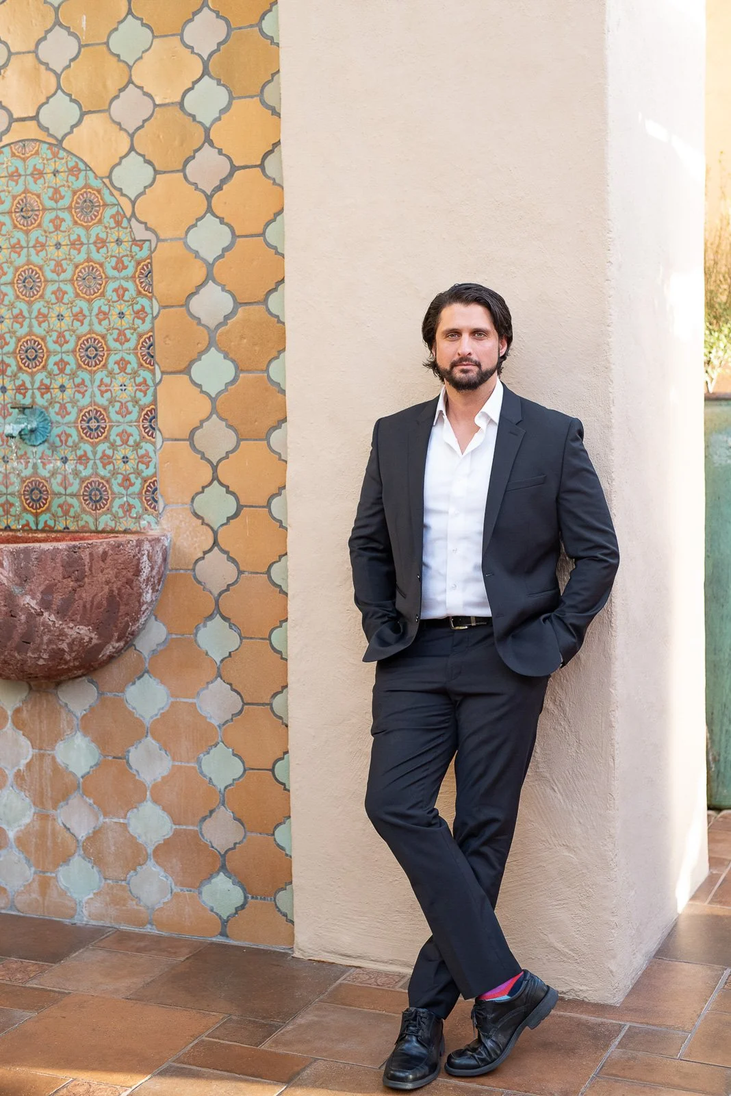 Male business professional leaning against architectural wall in outdoor environmental brand portrait.